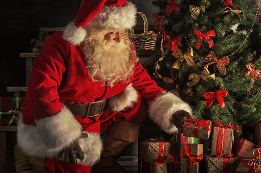 Istockphoto 491090202 170667a Santa Claus brought gifts for Christmas. Santa is placing gift boxes under Christmas tree
